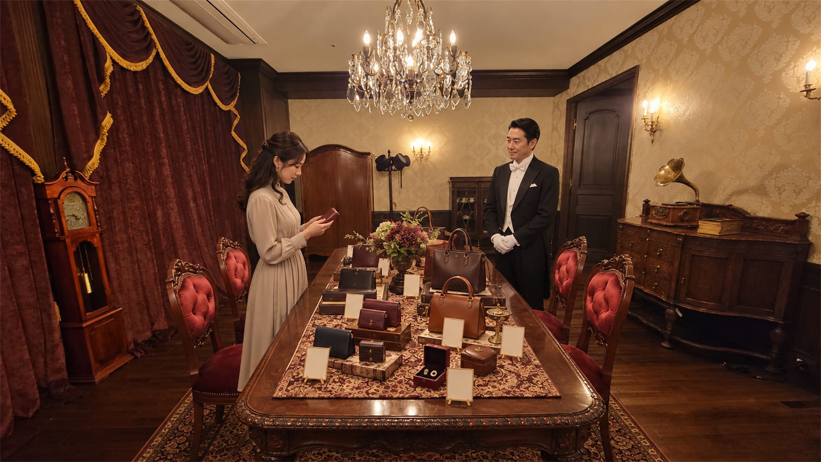 正餐の間の長い卓に革小物を並べたポップアップ展示。来場者が手に取り、執事が控える